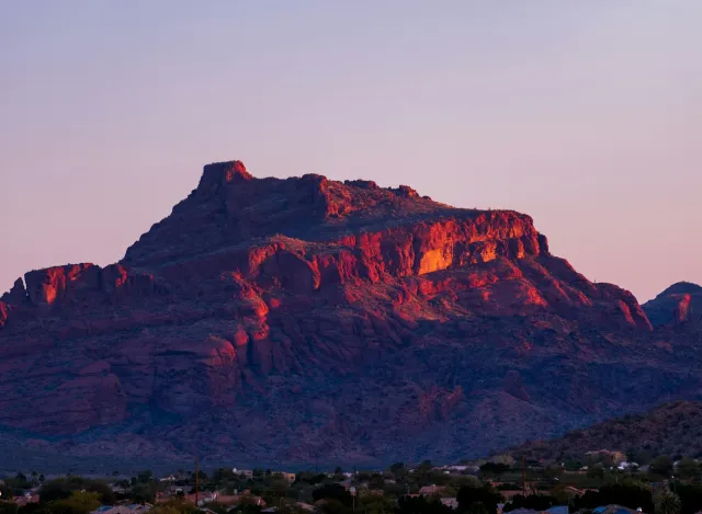 Sunset lights up red rock mountain with purple sky over desert town in the foreground.