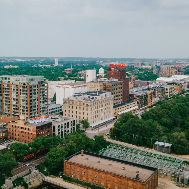 Aerial view of a cityscape with residential buildings, green trees, and industrial structures under a cloudy sky.