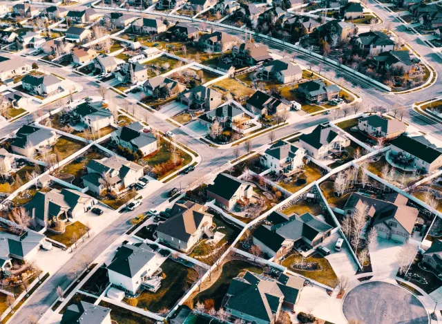 Aerial view of a suburban neighborhood with houses, roads, and lawns under clear daylight conditions.