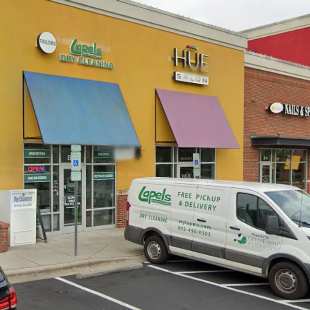Lapels Dry Cleaning storefront with blue awning and branded delivery van in front, next to HUE Salon and Nails & Spa.