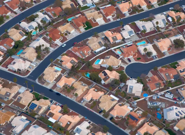 Aerial view of a suburban neighborhood with curved streets and beige-roofed houses, some with pools.