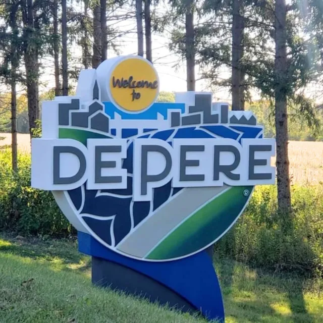 Welcome to De Pere sign with city skyline and nature background in a sunny outdoor setting