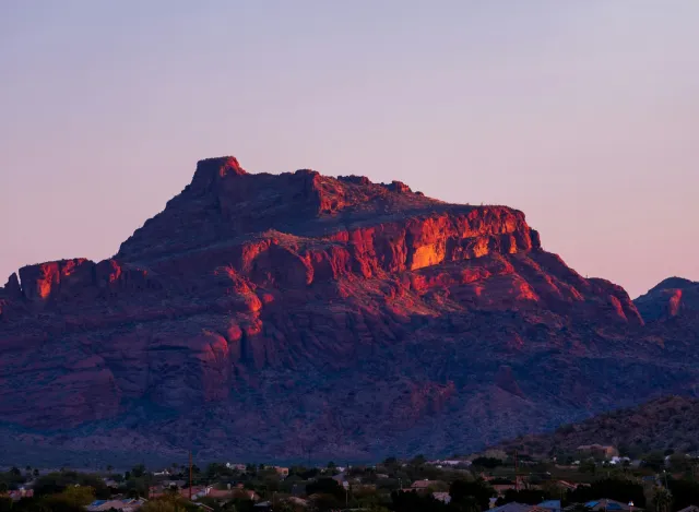 Sunset casts warm orange light on rugged desert mountain overlooking valley and small town below.
