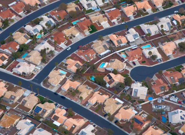 Aerial view of suburban neighborhood with curved streets, uniform houses, and some swimming pools visible.