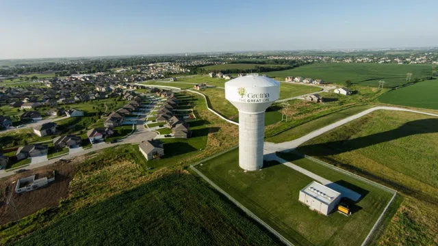 Aerial view of Gretna water tower and residential neighborhood surrounded by green fields under clear sky.