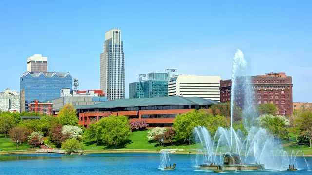 City skyline with modern buildings and a large fountain in foreground on a sunny day with blue sky.