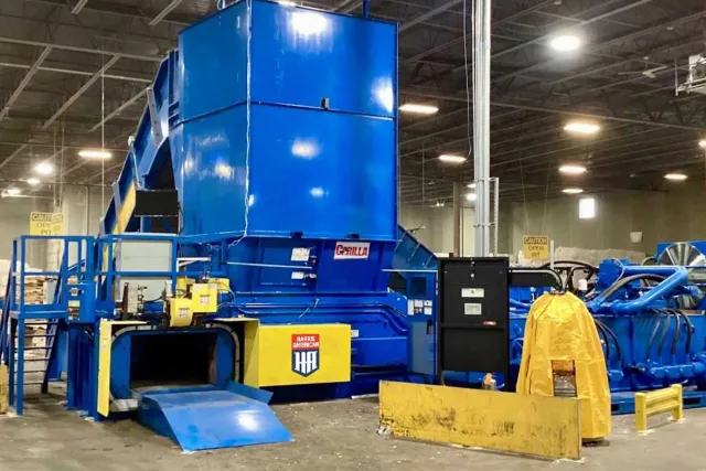 Large blue industrial machine with yellow safety barriers and railings inside a factory warehouse.