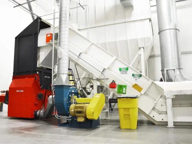 Industrial machinery with red and yellow components in a clean white factory space next to safety equipment and ducting.