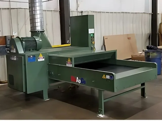 Large green industrial drying machine with conveyor belt inside a factory setting.