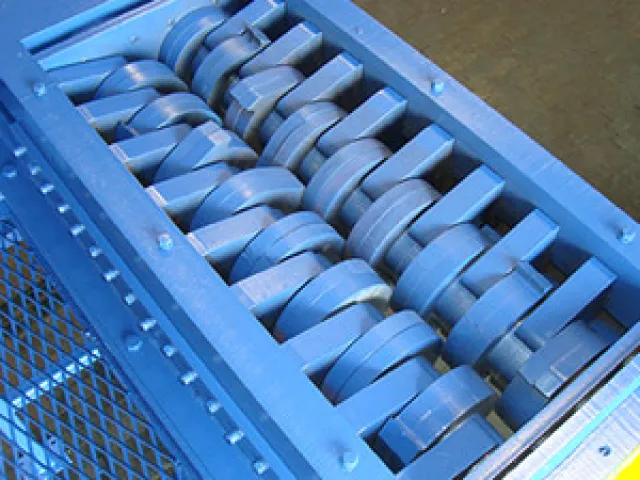 Close-up of blue industrial metal shredder with interlocking rotating blades inside a metal frame
