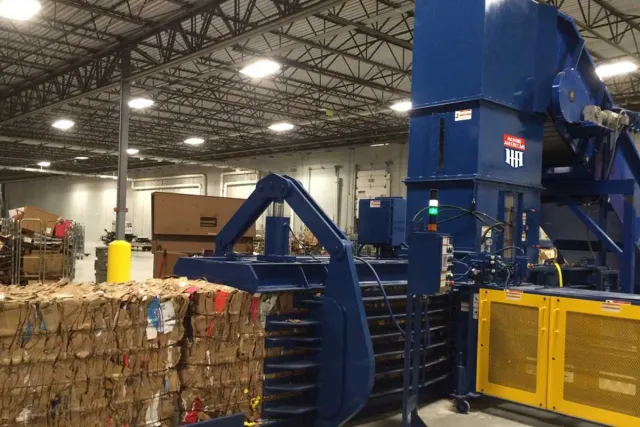 Industrial cardboard baler compresses recyclable cardboard into large compact bales in a warehouse setting