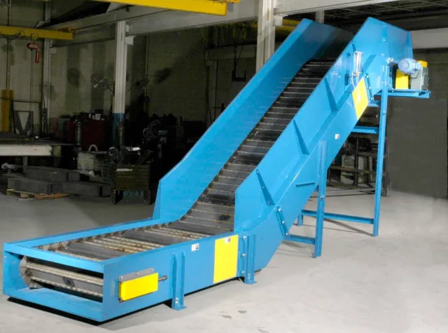 Blue industrial conveyor belt with metal rollers in a factory setting and 1-ton yellow overhead crane.