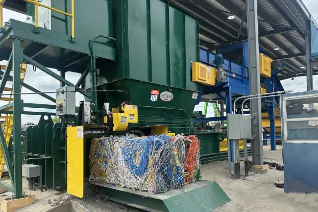 Industrial machine compressing a large bundle of mixed electrical wires and cables in a recycling facility.