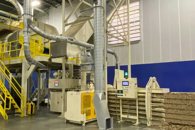 Industrial baling machine compressing recyclable cardboard and paper materials in a factory setting with ventilation pipes