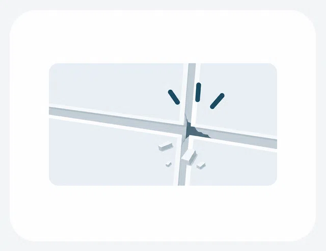Close-up of cracked light blue tiles with small broken pieces scattered near the fracture on a smooth surface.