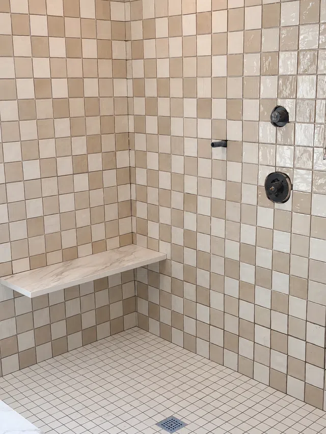 Beige tiled shower area with built-in corner bench and matte black fixtures including shower controls and spout.