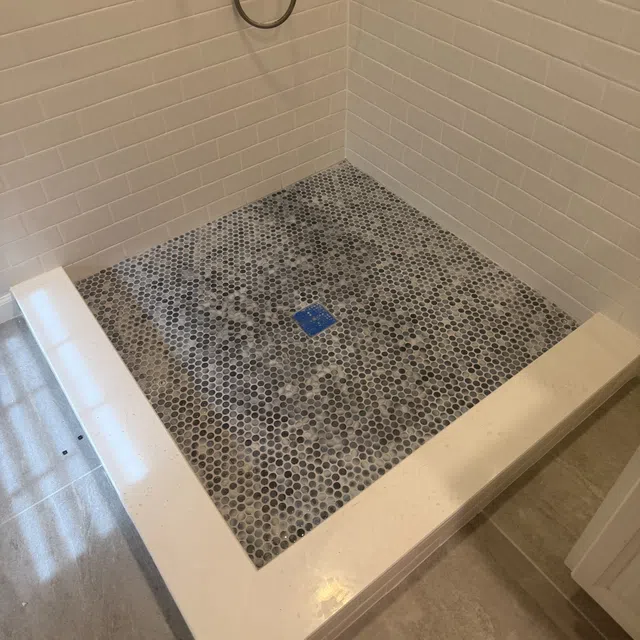 Bathroom shower with white subway tiles on walls and hexagonal mosaic tile flooring with a built-in drain.