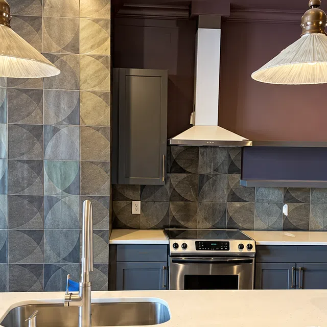 Modern kitchen with geometric tile backsplash, stainless steel stove and sink on white quartz countertop
