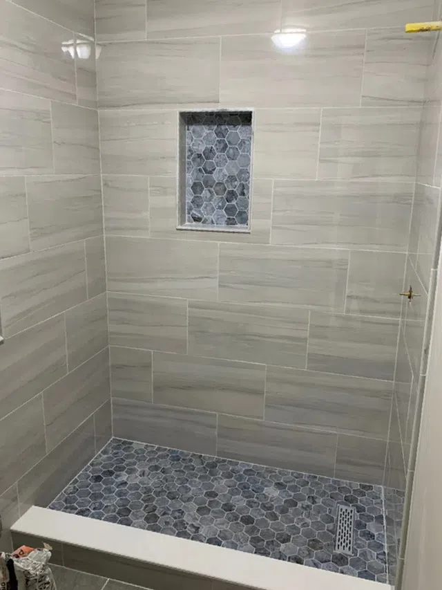 Modern shower with large rectangular wall tiles and hexagonal floor tiles with built-in niche.
