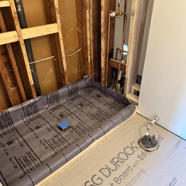 Partially constructed bathroom with USG Durock cement board flooring and waterproof membrane in shower area with exposed wooden studs.