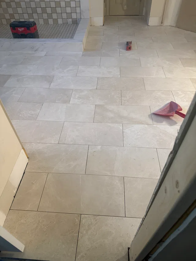 Light beige ceramic floor tiles freshly installed in a room under renovation with tools scattered around.