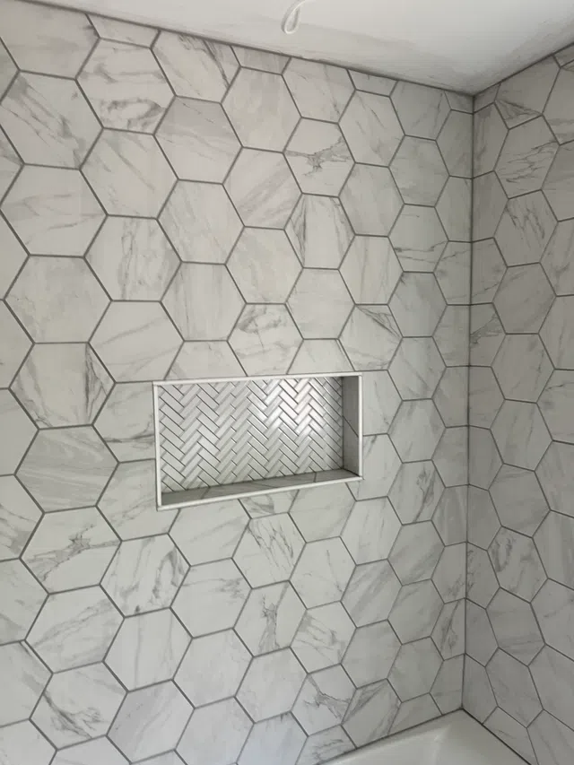 Bathroom wall with large hexagonal marble tiles and inset shelf with herringbone pattern tiles.