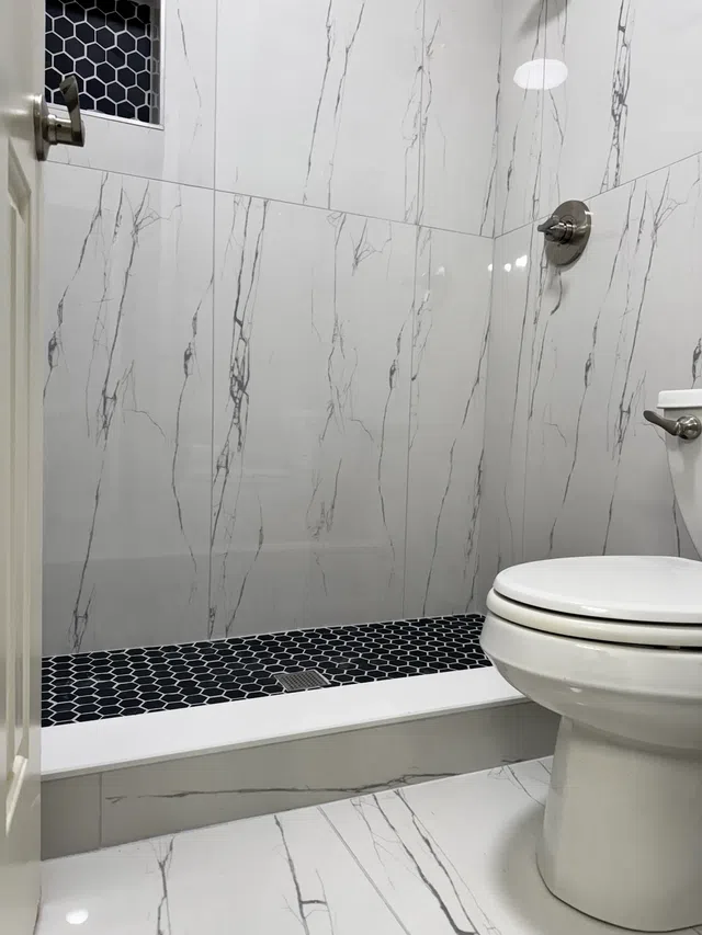 Clean modern bathroom with white marble walls, black hexagonal shower floor tiles, and a white toilet.