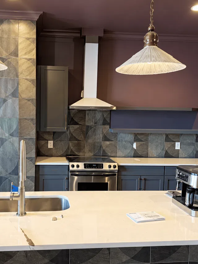 Modern kitchen with sleek stainless steel stove, geometric tile backsplash, white countertop, and hanging light fixture.
