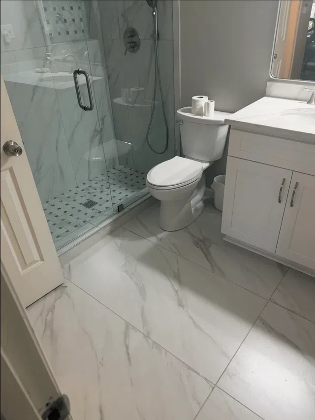 Modern bathroom with marble tile floor, glass shower enclosure, white toilet, and white vanity with sink.