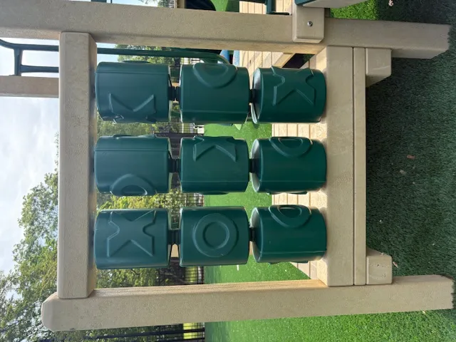 Outdoor tic-tac-toe game with large green rotating blocks on a beige frame in a park setting