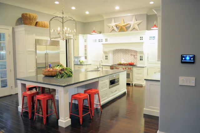 Bright modern kitchen with white cabinetry, large island, red stools, stainless steel appliances, and dark hardwood floors.