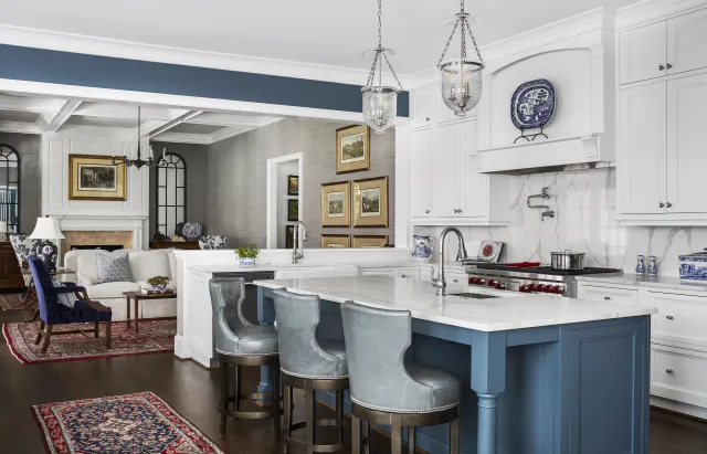 Modern kitchen with white cabinets, blue island, marble countertop, and adjacent living area with fireplace and rugs.