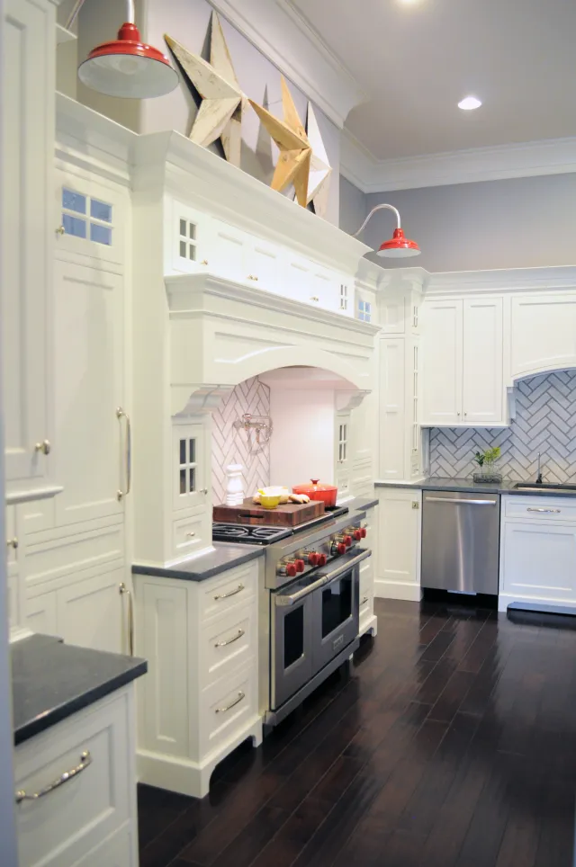 White kitchen with dark hardwood floors, stainless steel appliances, red accents, and star wall decor above stove
