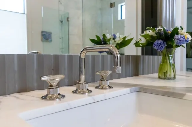 Modern chrome bathroom faucet and handles on marble countertop with fresh flowers in the background