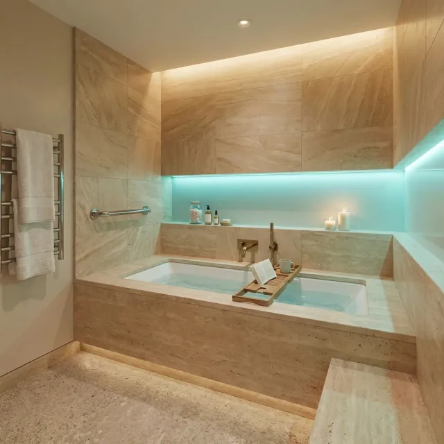 Modern bathroom with stone bathtub, underwater lighting, candles, towel rack, and bath caddy with book and cup
