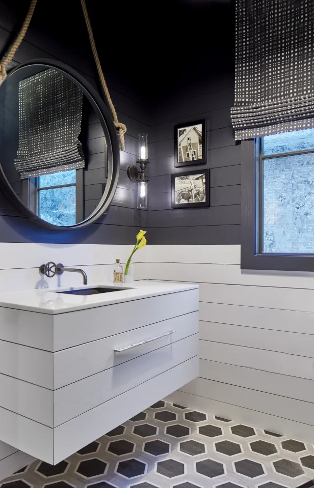 Modern bathroom with black and white shiplap walls, floating vanity, round mirror, and hexagon tile floor.