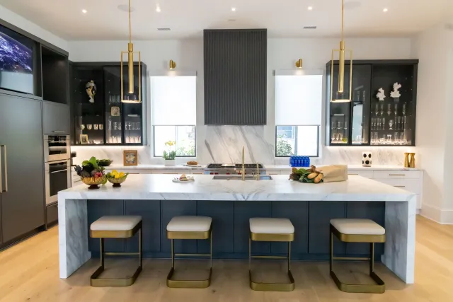 Modern kitchen with large marble island, four stools, black cabinetry, gold accents, and pendant lighting
