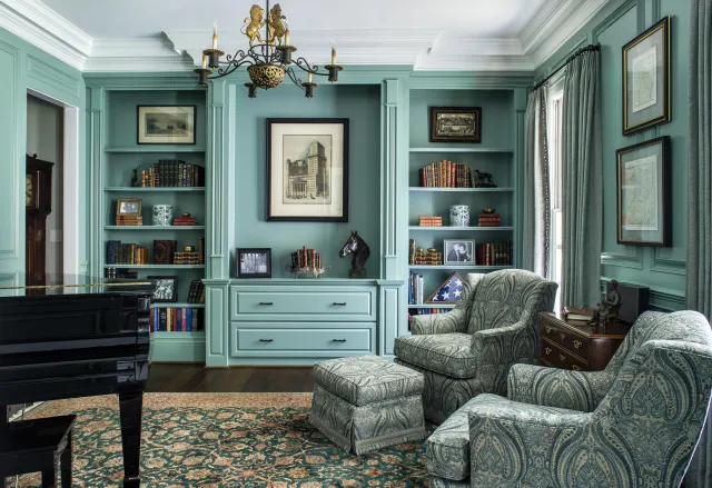 Elegant living room with teal built-in bookshelves, paisley armchairs, grand piano, and classic decor.