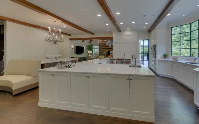 Spacious modern kitchen with large white island, hardwood floors, chandelier, and big windows overlooking greenery