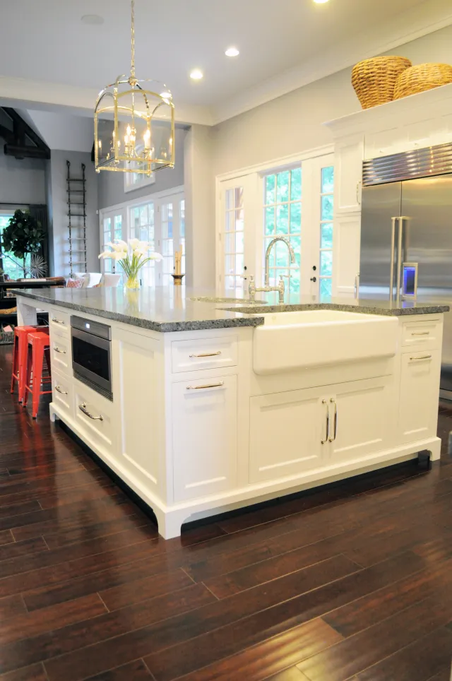 Modern kitchen with large white island, farmhouse sink, granite countertop, stainless steel fridge, and pendant light.