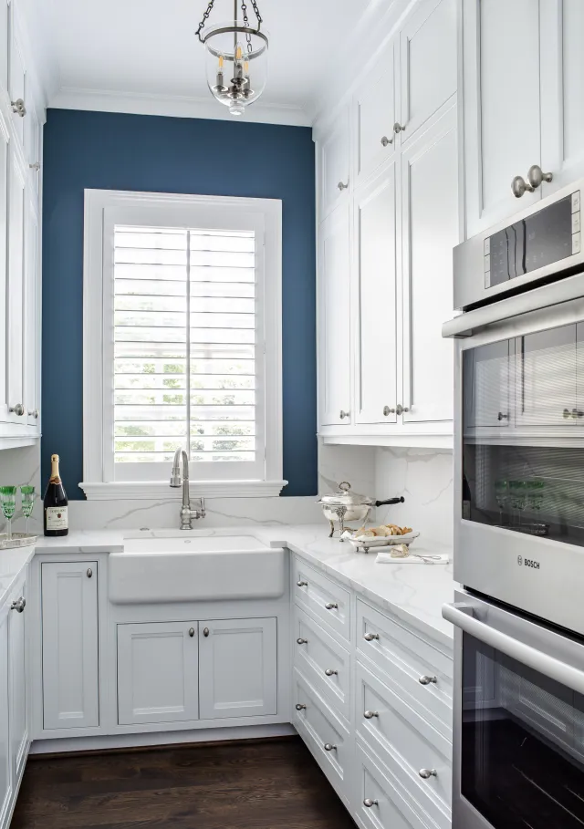 Bright modern kitchen with white cabinets, farmhouse sink, stainless steel oven, and blue accent wall