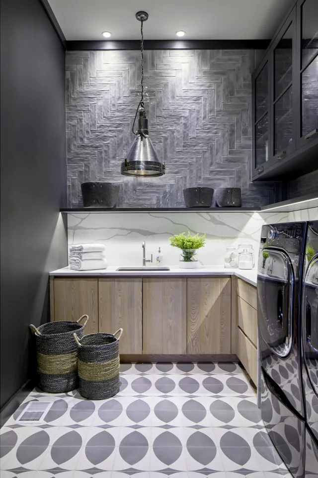 Modern laundry room with patterned floor tiles, wooden cabinets, black washer and dryer, and pendant light fixture.