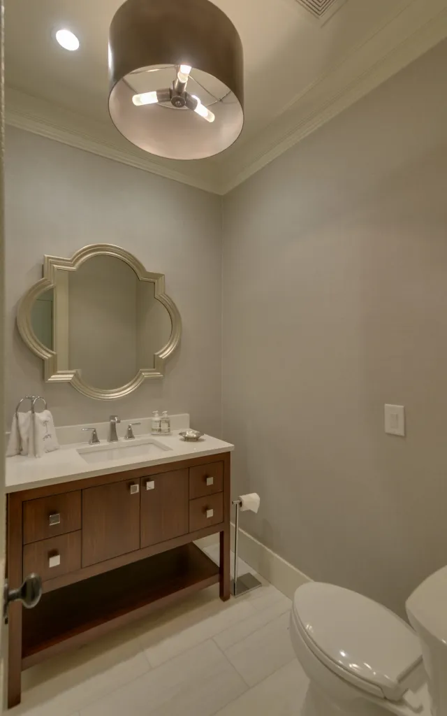 Modern bathroom with wooden vanity, decorative mirror, toilet, and overhead light fixture in neutral tones