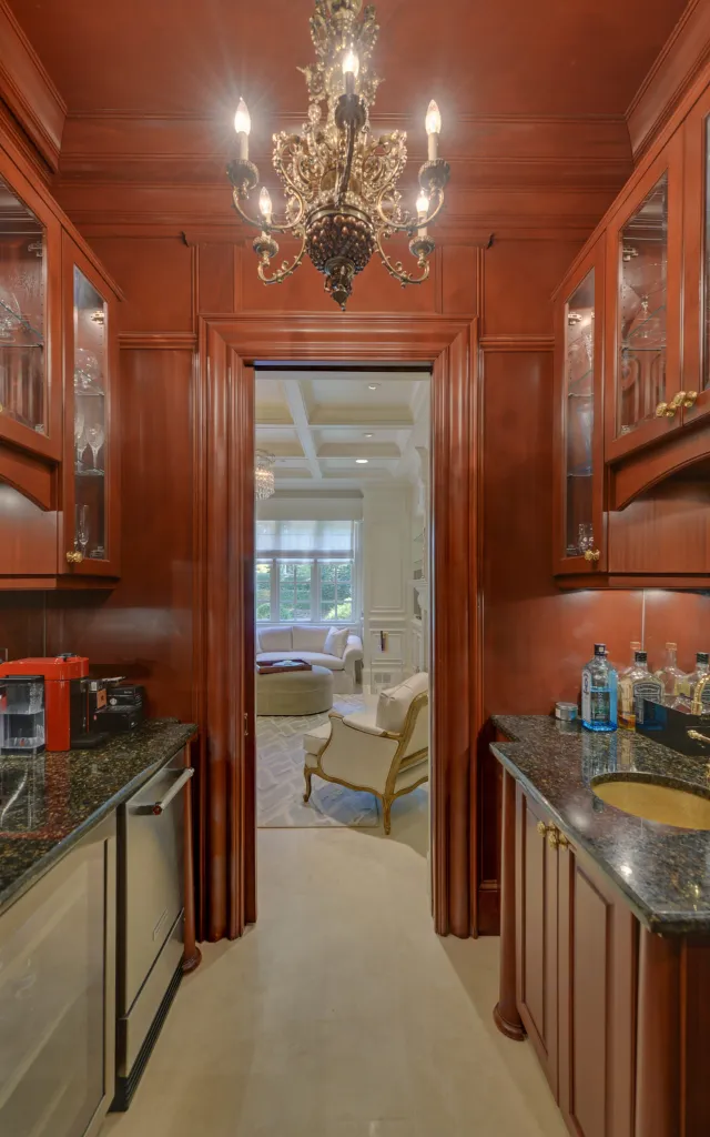 Luxurious wet bar with dark wood cabinets, granite countertops, chandelier, and view into elegant living room.