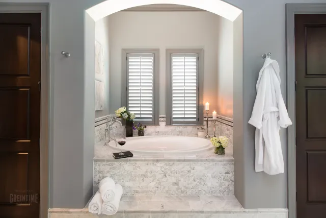 Luxurious marble bathtub with candles, flowers, white towels, and a bathrobe in a modern bathroom setting