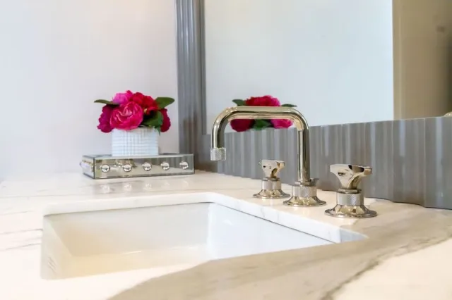 Modern bathroom sink with chrome faucet and vibrant pink flowers on marble countertop below a large mirror.