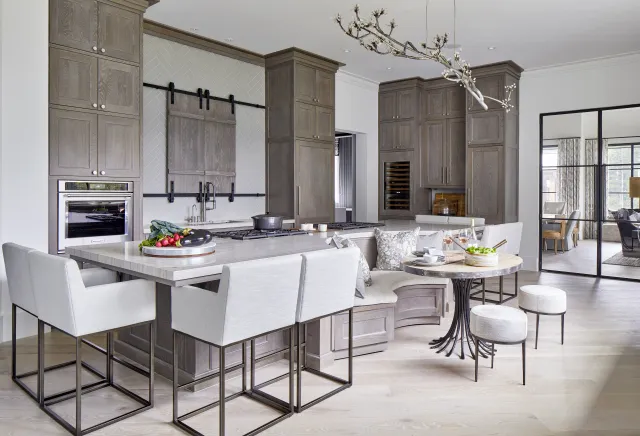 Modern kitchen with gray cabinetry, white island seating, a round dining table, and contemporary lighting fixture.