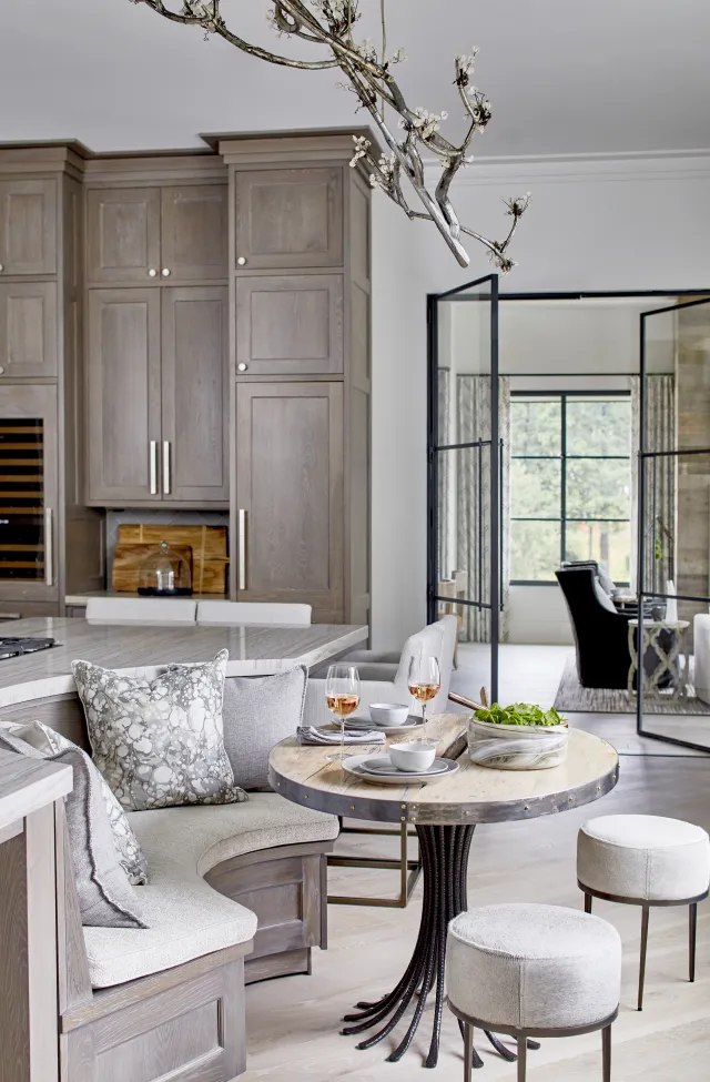 Cozy breakfast nook with curved cushioned bench, round wooden table, two stools, and kitchen cabinetry background.