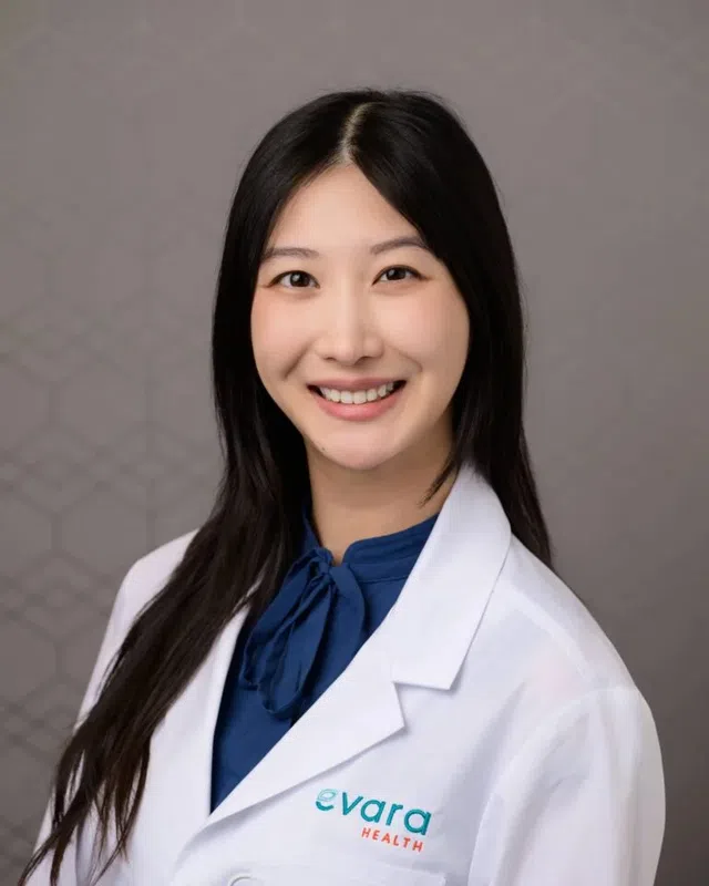 Smiling female healthcare professional wearing a white coat with Evara Health logo on a neutral background