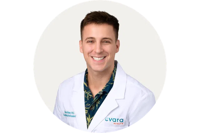 Smiling male doctor in white coat with Evara Health logo on a light background